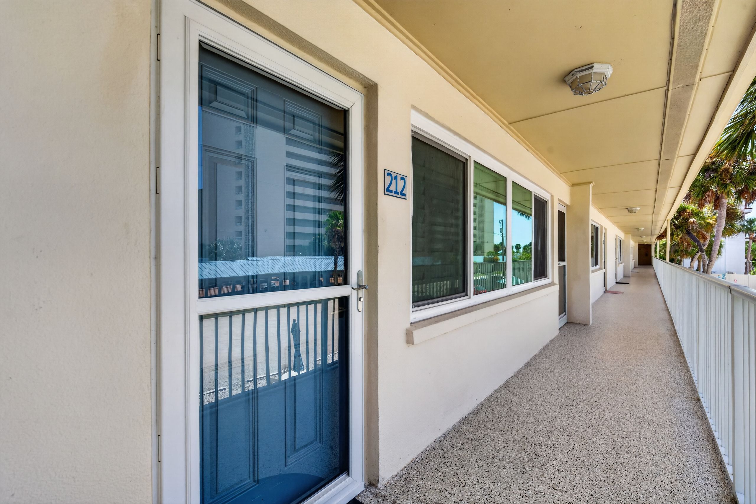 Un couloir bordé de fenêtres et de portes, une plaque portant le numéro « 212 », et une allée couverte.