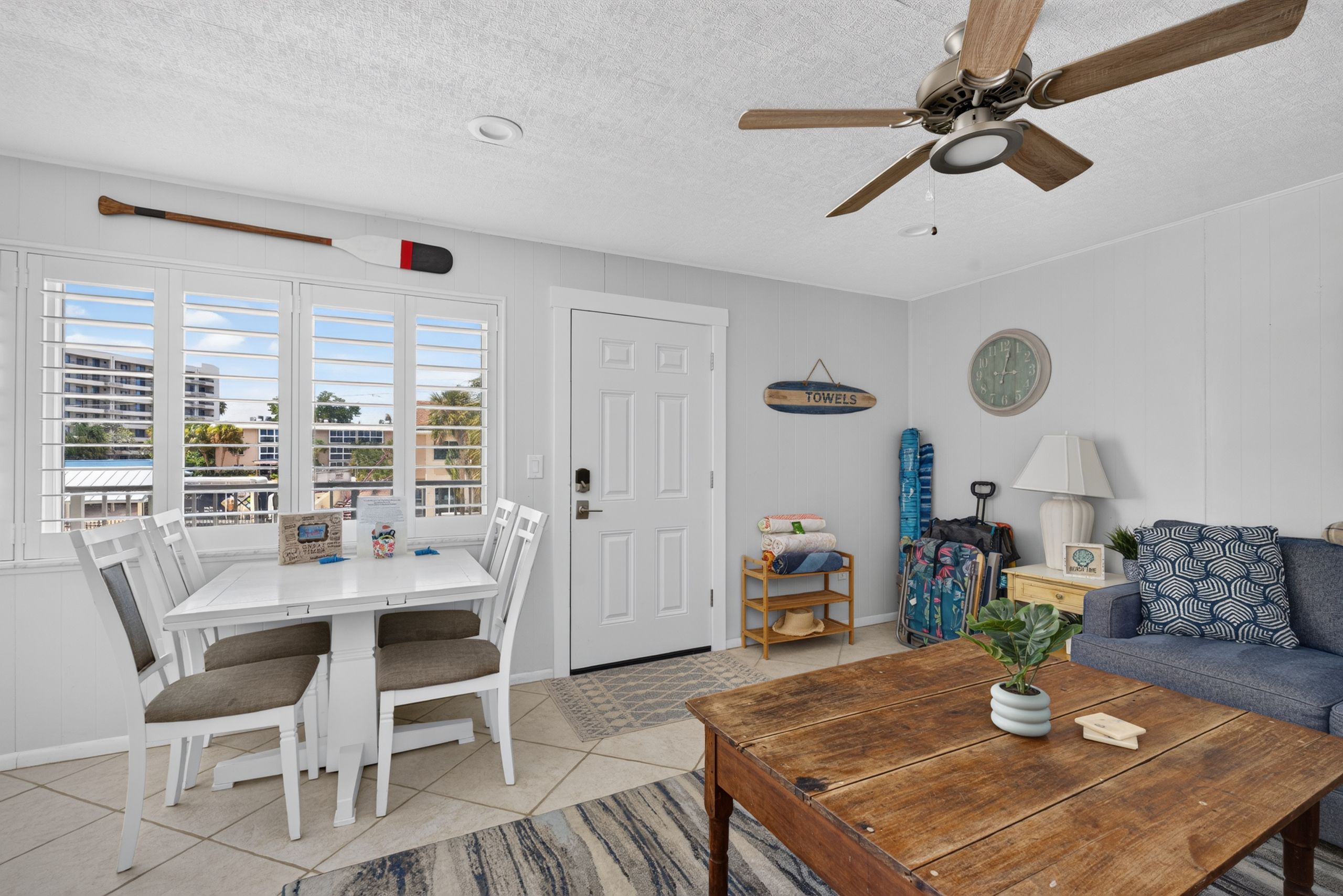 A room with a dining table, chairs, a ceiling fan, a sofa, a coffee table, and a view through the window.
