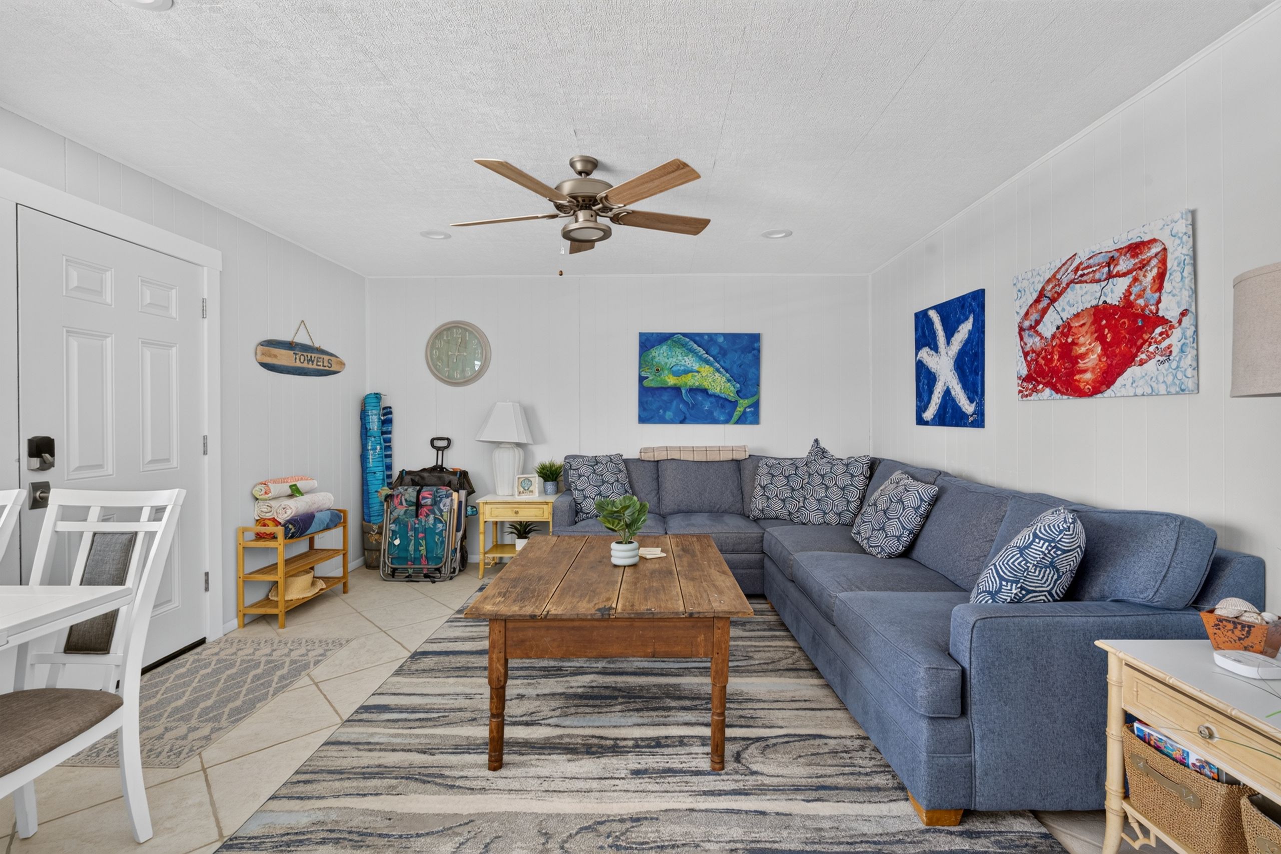A living room with a sofa, a wooden coffee table, a ceiling fan, and wall art.