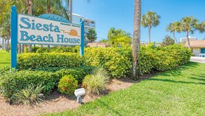 Schild für Siesta Beach House mit freiem Blick auf die umliegende Bepflanzung und Palmen.