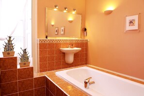 A bathroom with a large bathtub, a sink, and a mirror above the sink. There are potted plants on the floor and a framed picture on the wall. - Luxury Central Old Town Suite Edinburgh (Edinburgh)