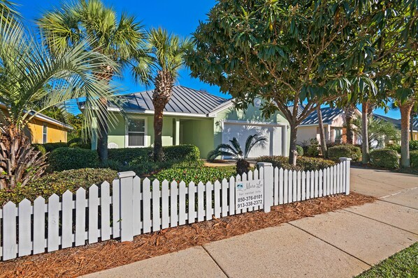 A residential property with a white picket fence, a well-maintained garden, and a house with a green roof.