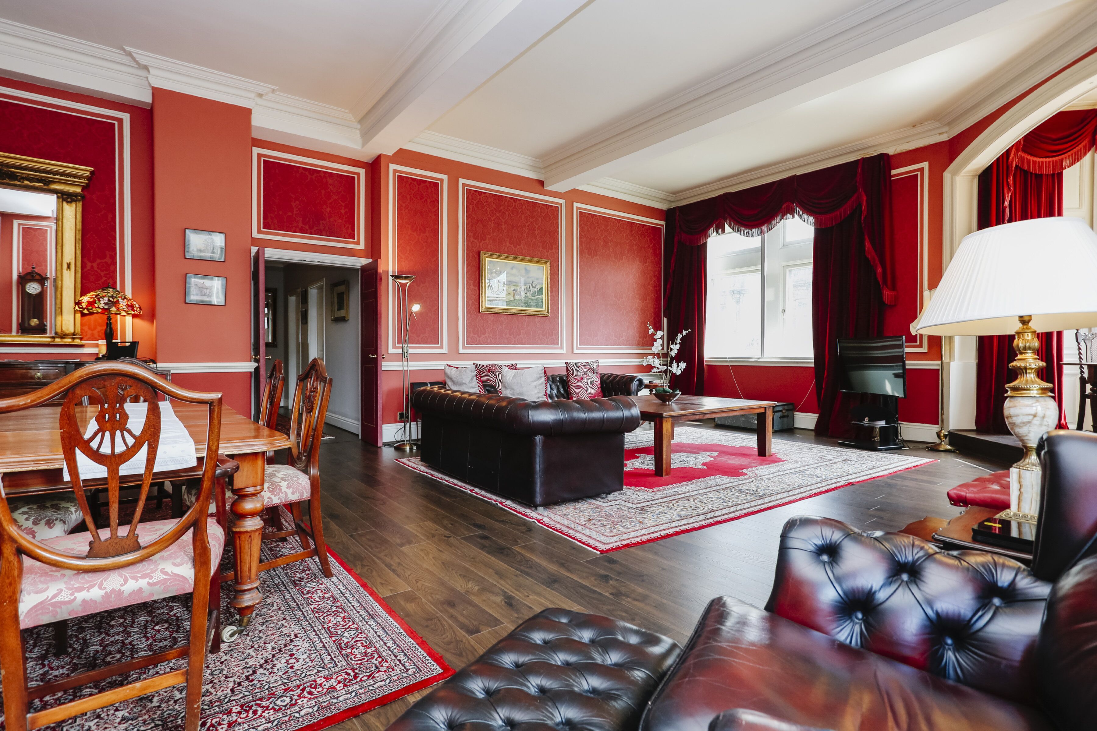 A spacious living room with a fireplace, red walls, and a large window with curtains.