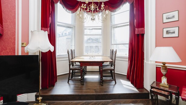 A dining area with a wooden table and chairs, red curtains, and a chandelier. - Gorgeous Royal Mile Mansion Apartment (Edinburgh)