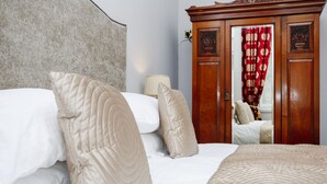 A neatly made bed with multiple pillows and a patterned blanket, a wooden wardrobe with a mirror, and a lamp on a bedside table. - Gorgeous Royal Mile Mansion Apartment (Edinburgh)