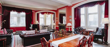 A traditional living room with a fireplace, red curtains, and a dining area with wooden furniture.