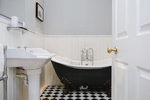 A bathroom with a white sink, a black bathtub, and a checkered floor.