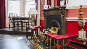 A room with a fireplace, red upholstered chairs, a table with chairs, and a chandelier. - Gorgeous Royal Mile Mansion Apartment (Edinburgh)
