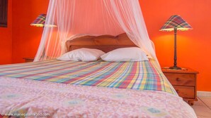 Ein Bett mit bunter, gestreifter Bettdecke, einem Holz-Kopfteil und weißen Kissen. Zwei Nachttische mit Karotten-Lampenschirmen sind vorhanden.