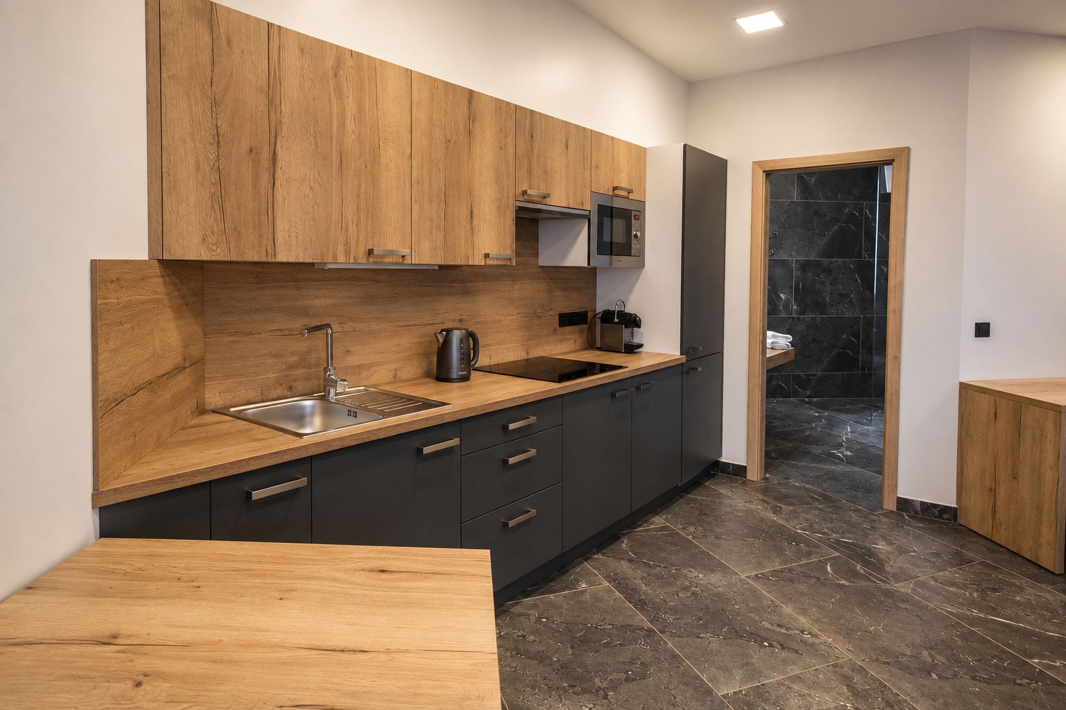 Una cocina moderna con armarios de madera, un lavamanos de acero inoxidable y un hervidor eléctrico negro.