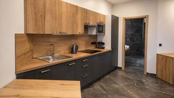 Una cocina moderna con armarios de madera, un lavamanos de acero inoxidable y un hervidor eléctrico negro.
