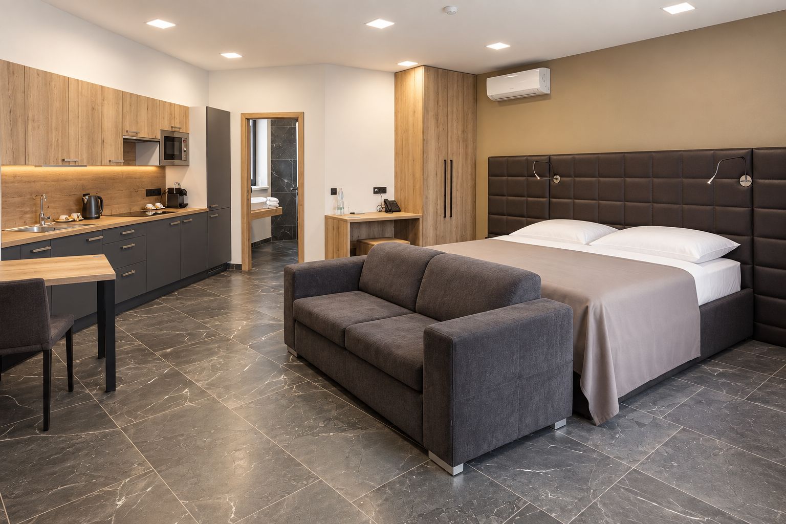 Ett modernt hotellrum med en säng, en soffa, ett skrivbord och ett litet kök.