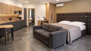 Ett modernt hotellrum med en säng, en soffa, ett skrivbord och ett litet kök.