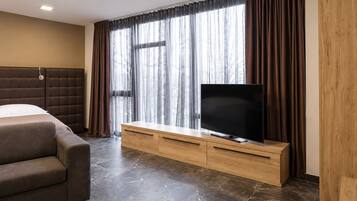 Ein Hotelzimmer mit Bett, einer Couch, einem Fernseher auf einer Holzkonsole und einem großen Fenster mit Vorhängen.