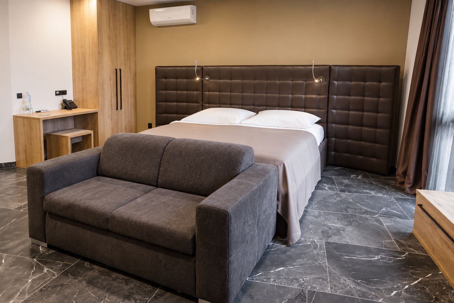 A hotel room with a bed, a sofa, a wooden cabinet, and a marble floor.