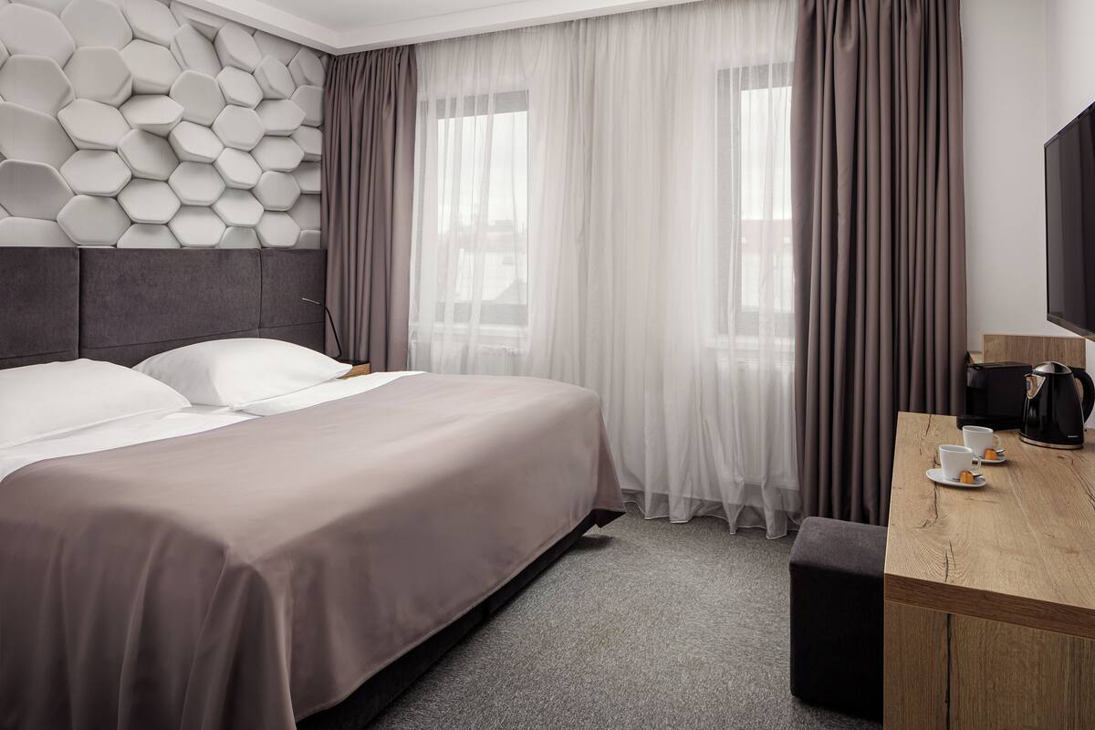 A hotel room with a bed, a desk with a coffee maker, and a TV.
