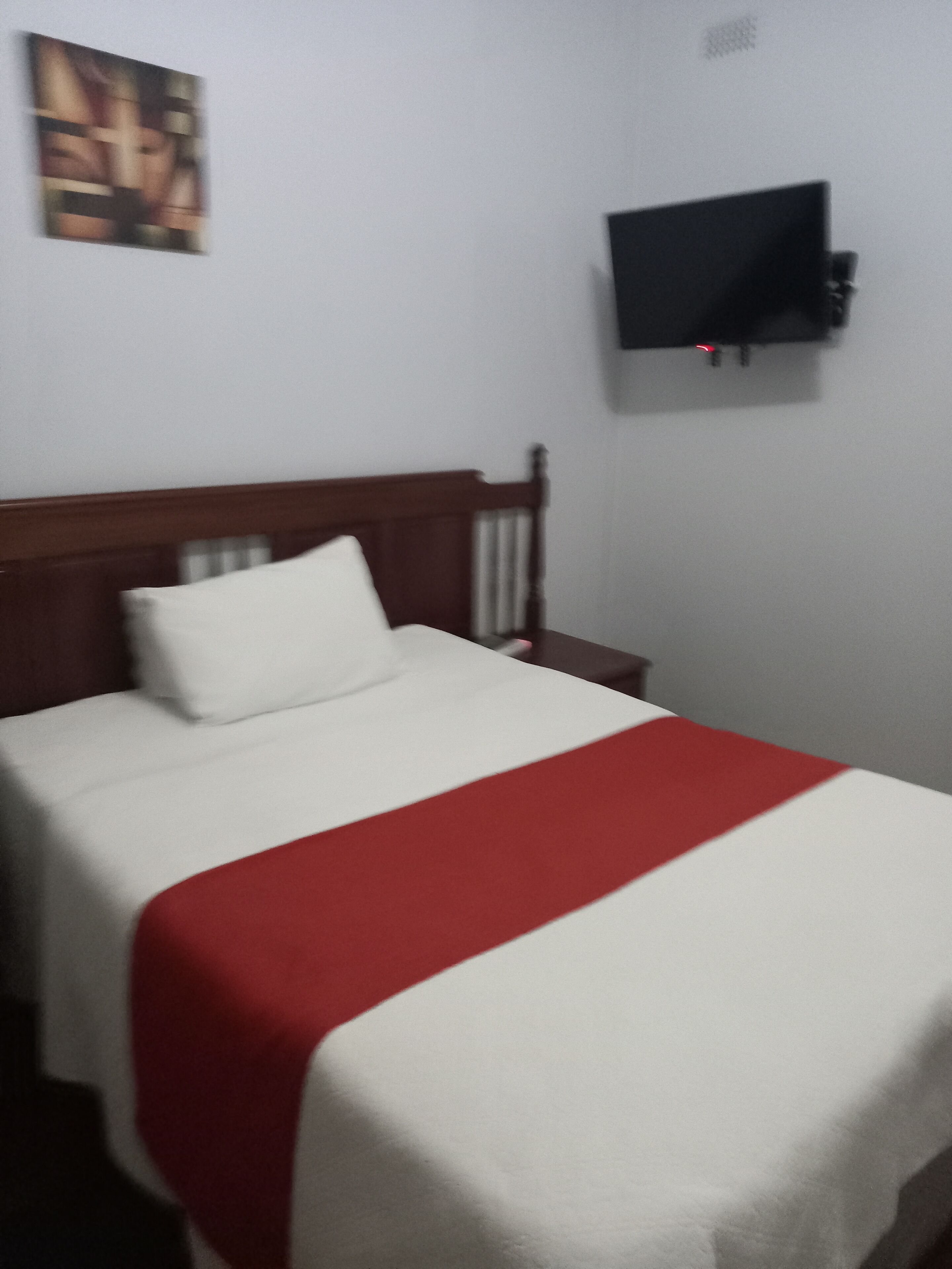 Un lit avec une couvre-lit blanche et rouge, une tête de lit en bois et un oreiller blanc.