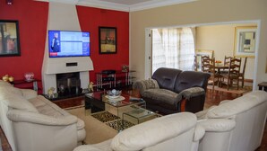 A living room with a fireplace, a television, and a dining area with chairs and a table. - Las Palmas Guest House (Harare)