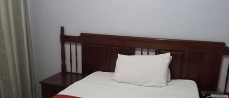 Una cama bien hecha con una colcha blanca y roja, un cabecero de madera y un pequeño cuadro en la pared.