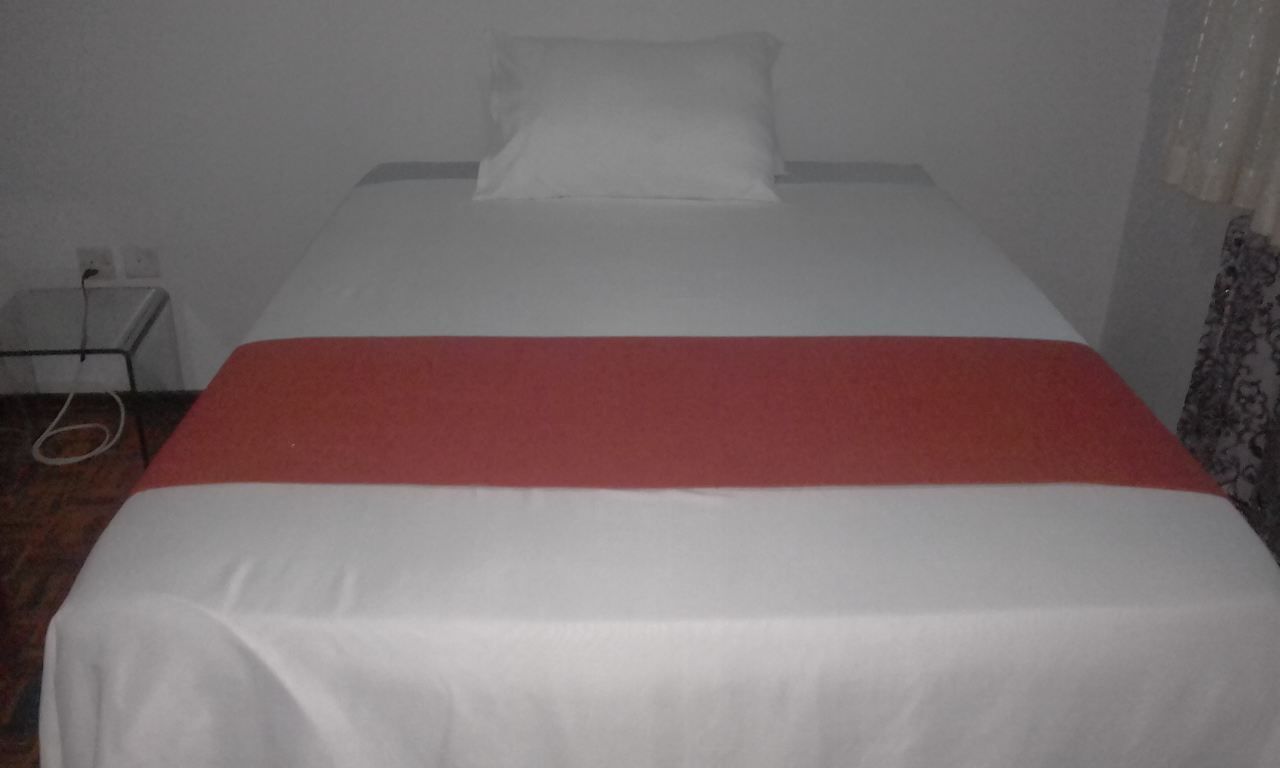 A bed with a white and red bedspread in a room with white walls and a small bedside table.
