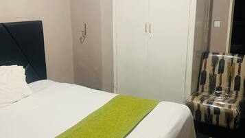 A hotel room with a bed, a wardrobe, a chair, and a carpet.