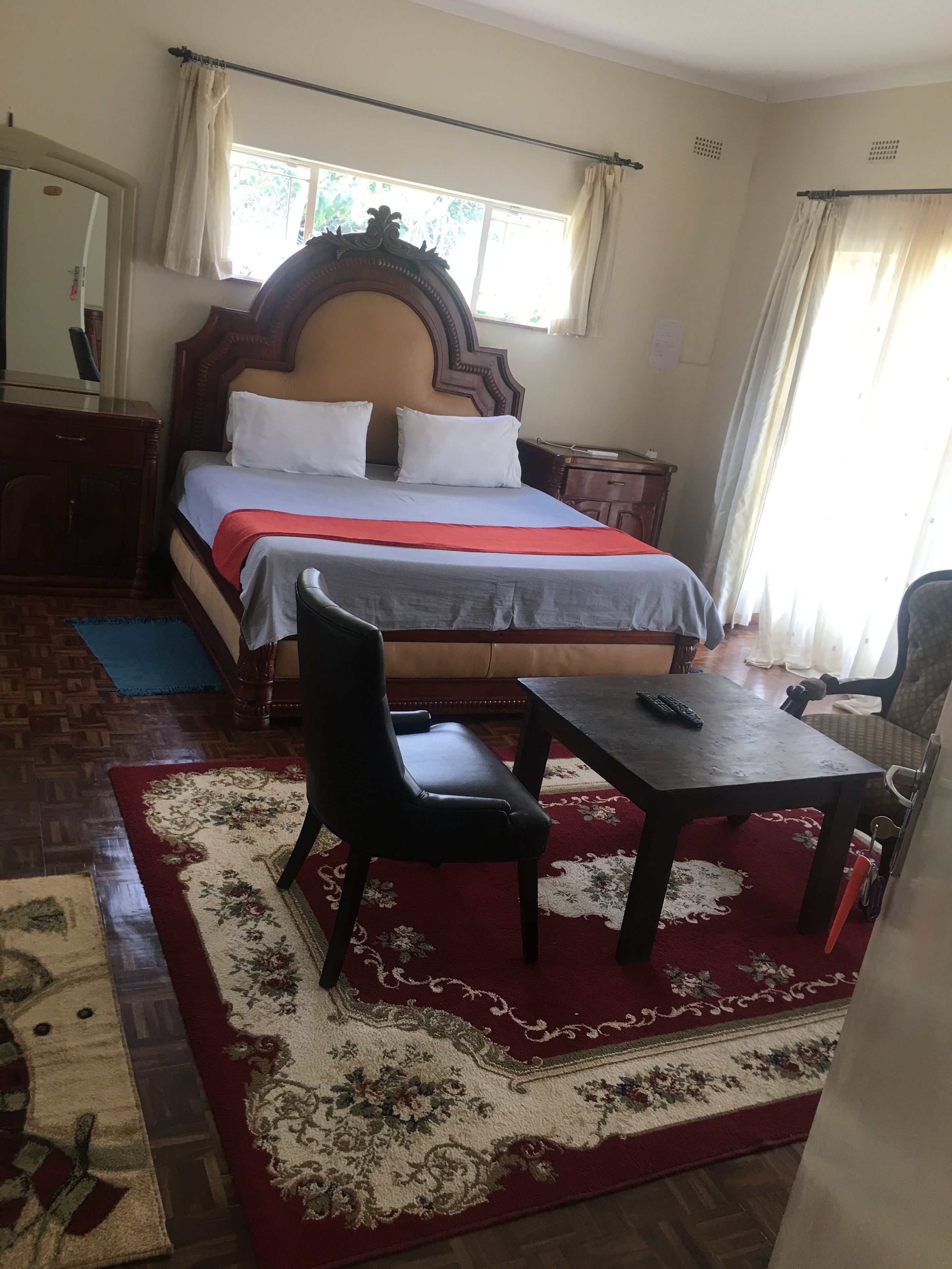 A bedroom with a bed, a nightstand, a chair, a table, and a window with curtains.