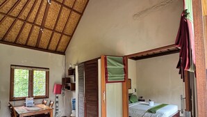A room with a thatched roof, a bed, a dining table with chairs, and a small table with a lamp. - Upper Level 1BR Apartment with Shared Pool (Ubud)