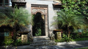 A traditional stone entrance with steps leading up to a decorative archway, surrounded by lush greenery and stone statues. - Upper Level 1BR Apartment with Shared Pool (Ubud)