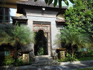 A traditional stone entrance with steps leading up to a decorative archway, surrounded by lush greenery and stone statues. - Upper Level 1BR Apartment with Shared Pool (Ubud)