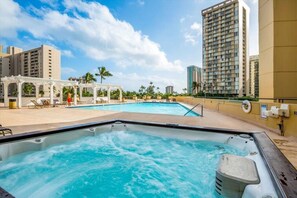 A rooftop pool area with a hot tub, lounge chairs, and a pergola.