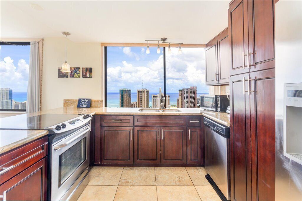 A kitchen with a large window, wooden cabinets, a stove, and a dishwasher.