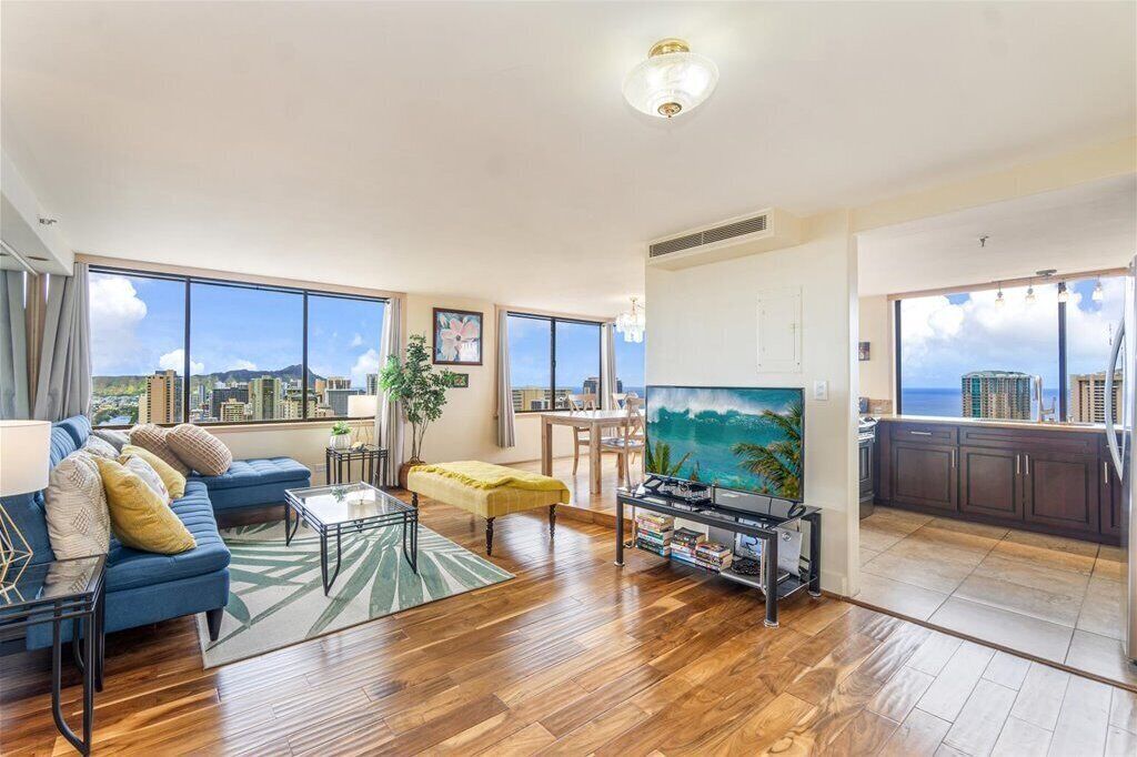 Ein geräumiges Wohnzimmer mit großem Fernseher, Holzböden, einem blauen Sofa und Blick auf die Stadt.
