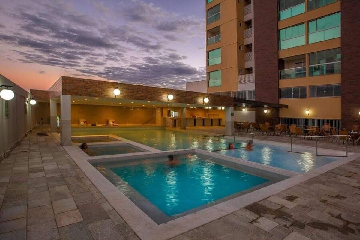 A rooftop swimming pool with multiple lanes, surrounded by lounge chairs and a building with a brick facade.