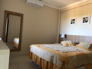 A hotel room with a large bed, a bedside table, a lamp, and a mirror. - Piazza Di Roma - Reserve Caldas (Caldas Novas)