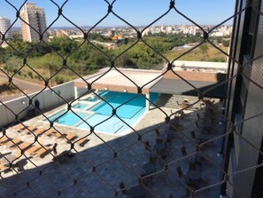 A chain-link fence overlooking a swimming pool with a cityscape in the background. - Piazza Di Roma - Reserve Caldas (Caldas Novas)