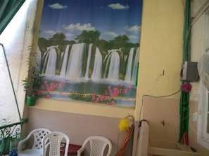 Une pièce décorée d’une fresque représentant des cascades, avec une plante verte et une fenêtre agrémentée d’un ventilateur et de rideaux.