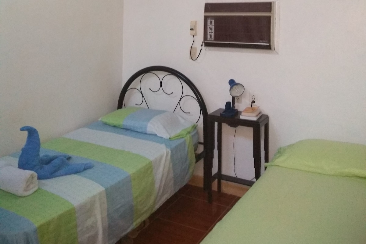 Une chambre avec deux lits simples, un ventilateur de plafond, une fenêtre avec vue et un climatiseur fixé au mur.