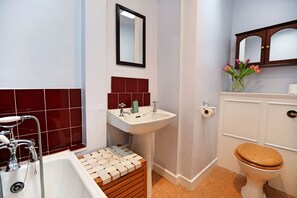 A bathroom with a bathtub, sink, mirror, toilet, and a vase with flowers. - Wonderful Central Edinburgh Apartment (Edinburgh)