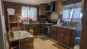 A kitchen with wooden cabinets, a stove, a sink, and a dining area with a table and chairs. - Kozy Korner will be your home away from home to refresh and rest when traveling. (Midpines)