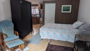 A bedroom with a bed, a chair, a wardrobe, a desk, and a door leading to a kitchen. - Kozy Korner will be your home away from home to refresh and rest when traveling. (Midpines)