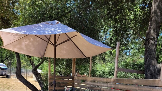 An outdoor seating area with a table and chairs under a large umbrella, a grill, and a gas cylinder. - Kozy Korner will be your home away from home to refresh and rest when traveling. (Midpines)