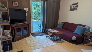 A living room with a wooden TV stand, a red sofa, a small wooden table, and a bookshelf. - Kozy Korner will be your home away from home to refresh and rest when traveling. (Midpines)