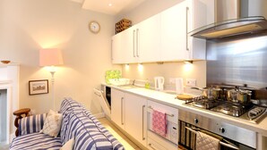 A modern kitchen with white cabinets, a stainless steel stove, and a dining area with a striped sofa. - Fantastic Edinburgh Apartment (Edinburgh)