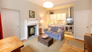A living room with a fireplace, a striped sofa, a wooden table, and a kitchen in the background. - Fantastic Edinburgh Apartment (Edinburgh)