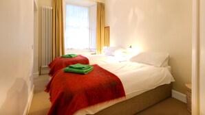 A hotel room with two beds, a radiator, a window with curtains, and a lamp on the nightstand. - Fantastic Edinburgh Apartment (Edinburgh)
