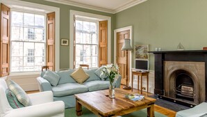 A living room with a light blue sofa, a wooden coffee table, and a fireplace. - Quality Stay 3-Bedroom Apartment (Edinburgh)