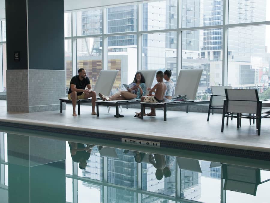 A pool area with lounge chairs and a view of the cityscape through large windows.