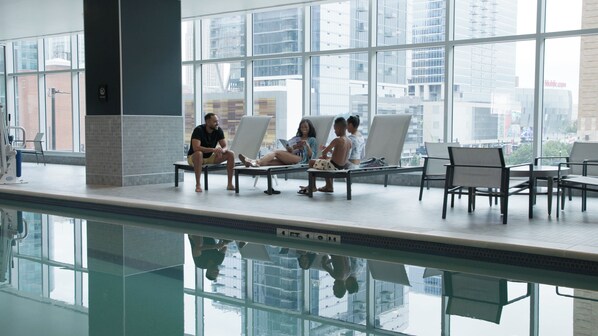 A pool area with lounge chairs and a view of the cityscape through large windows.