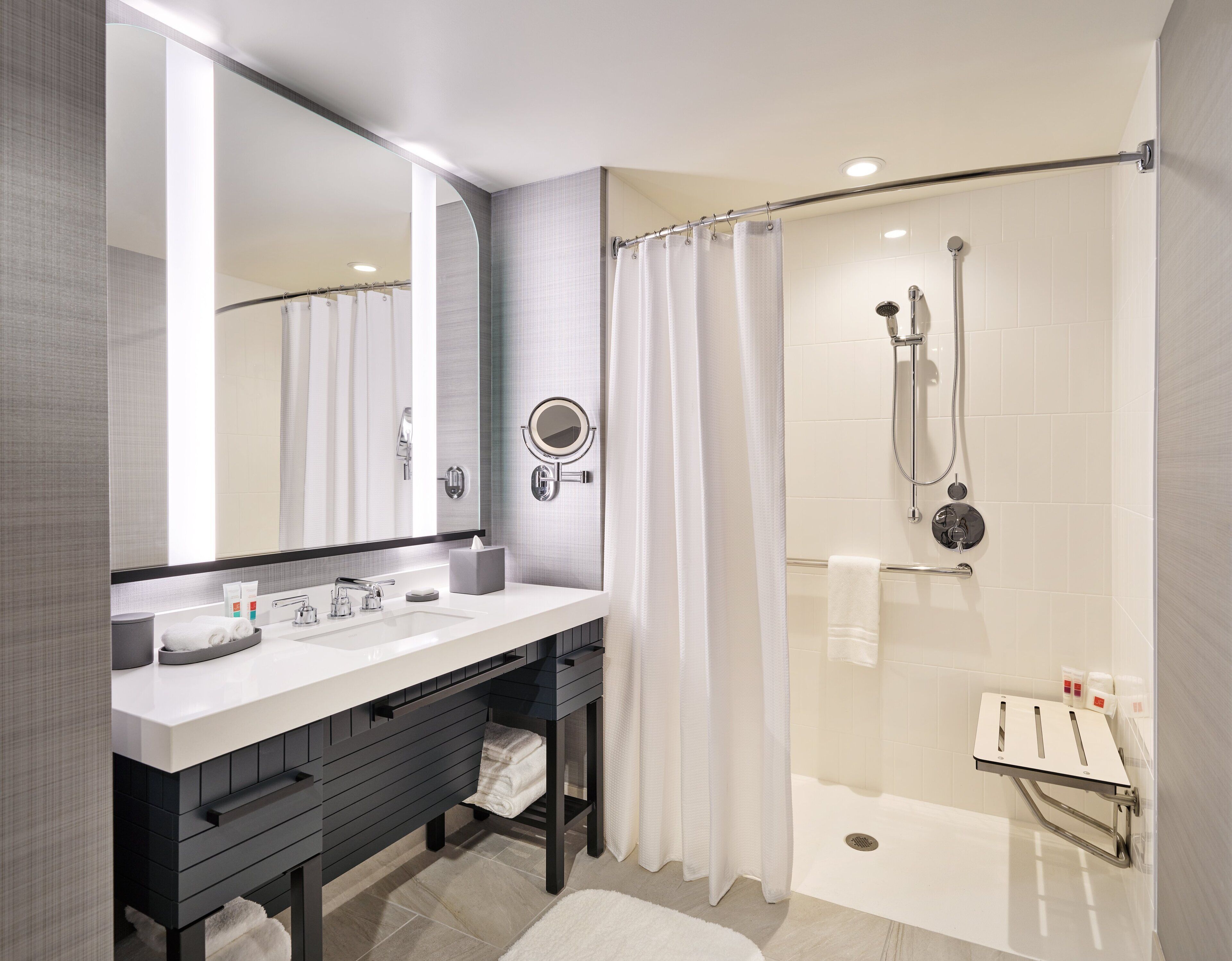 A modern bathroom with a double sink vanity, a large mirror, a shower with a glass door, and a towel rack.