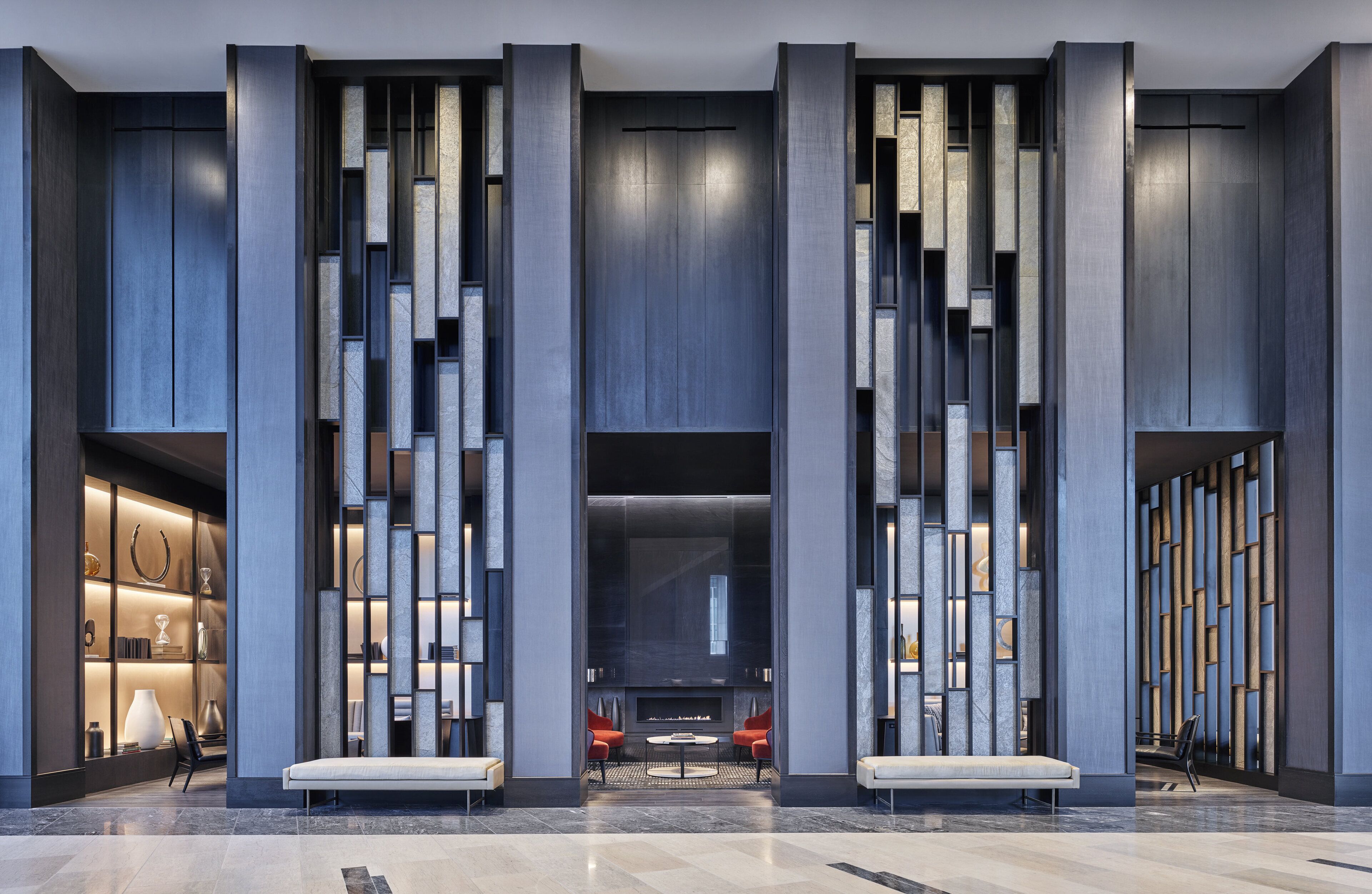 A modern lobby with a central fireplace, seating areas, and a display of decorative items.